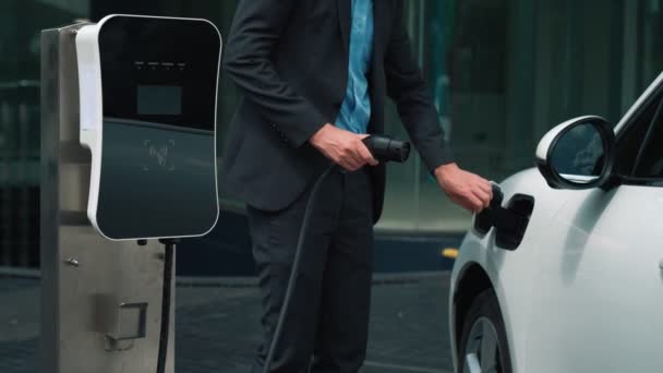 プログレッシブビジネスウーマン市内中心部を走行する前に充電ステーションから彼の電気自動車に充電器プラグをインストールします 持続可能でクリーンなエネルギーを動力とする環境に優しい充電式車 — ストック動画