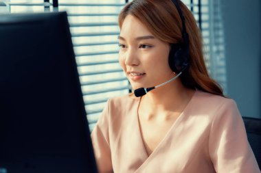 Competent female operator working on computer and while talking with clients. Concept relevant to both call centers and customer service offices.