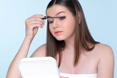 Closeup portrait of young charming applying makeup eyeshadow on her face with brush, mascara with flawless smooth skin for beauty concept.