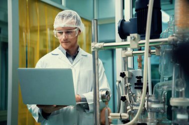 CBD yağ çıkarıcısının yanında dizüstü bilgisayarla çalışan eczacı bilim adamı ve tıbbi esrar ürünleri üretmek için kullanılan bilimsel bir makine.
