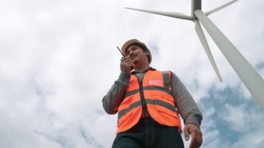 Gökyüzü arka planına sahip bir rüzgar türbini üzerinde çalışan mühendis. Yenilenebilir ve sürdürülebilir enerjinin gelecekteki üretimi için yenilikçi bir ideal. Rüzgar türbininden enerji üretimi.