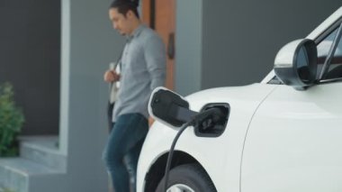 Adamın biri evinde elektrikli araç şarj aletinin fişini çekiyor. İlerici bir yaşam tarzında elektrikli araçların kullanımı, temiz ve sağlıklı bir çevreye katkıda bulunur..