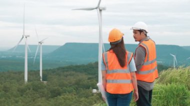 Erkek ve kadın mühendisler kırsal kesimdeki bir tepenin tepesinde ya da dağda rüzgar çiftliğinde çalışıyorlar. Yenilenebilir ve sürdürülebilir enerjinin gelecekteki üretimi için yenilikçi idealler.