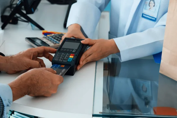 Payment by credit card with payment terminal in qualified drugstore or hospital. Modern payment of electric money. Closeup customer purchase medication in pharmacy with credit card on pos.