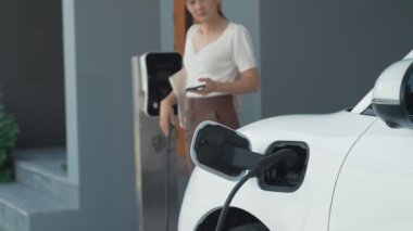 Evinde şarj edilen elektrikli bir araçla işten yeni dönen modern bir kadının ilerici yaşam tarzı. Elektrikli araç, sürdürülebilir temiz enerjiyle çalışıyor..