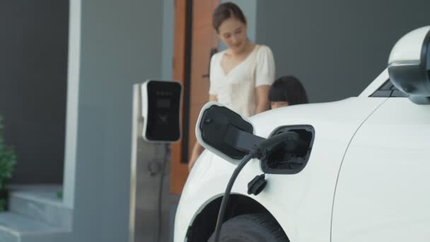 自宅で充電されている電気自動車で学校から戻ったばかりの母親と娘の進歩的なライフスタイル 持続可能なクリーンエネルギーを動力とする電気自動車 — ストック動画