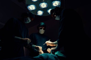 Steril ameliyathanedeki hastaya ameliyat yapan cerrahi ekip. Bir lambanın yaktığı ameliyathanede, profesyonel ve kendinden emin bir cerrahi ekip bilinçsiz bir hastaya tıbbi bakım sağlar..