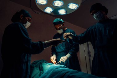 Steril ameliyathanedeki hastaya ameliyat yapan cerrahi ekip. Bir lambanın yaktığı ameliyathanede, profesyonel ve kendinden emin bir cerrahi ekip bilinçsiz bir hastaya tıbbi bakım sağlar..