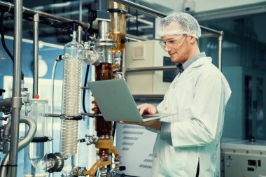 CBD yağ çıkarıcısının yanında dizüstü bilgisayarla çalışan eczacı bilim adamı ve tıbbi esrar ürünleri üretmek için kullanılan bilimsel bir makine.
