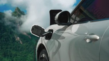 Temiz çevre için temiz enerjinin yol açtığı ilerici elektrikli araba kavramının arka planı olarak dağın tepesinde bulutun zaman kavramının yer aldığı doğal manzara. EV araba şarj istasyonunda şarj oluyor..