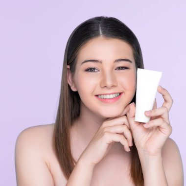 Young charming girl with natural beauty, perfect smooth skin hold lotion, cream, moisturizer tube. Beautiful girl show skincare product smiling on isolated background.