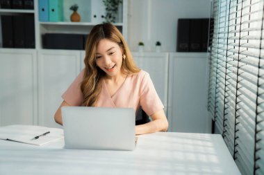 A young Asian female employee sitting at her desk in her office, sitting at desktop in workstation.