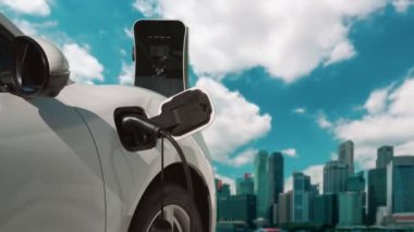 Elektrikli araç, EV araba şehir merkezindeki şarj istasyonunda şarj oluyor. Etrafı yüksek gökdelenlerle çevrili. Çevre dostu yenilikçi temiz enerji kavramı.