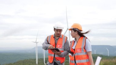 Erkek ve kadın mühendisler kırsal kesimdeki bir tepenin tepesinde ya da dağda rüzgar çiftliğinde çalışıyorlar. Yenilenebilir ve sürdürülebilir enerjinin gelecekteki üretimi için yenilikçi idealler.