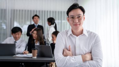 Portrait of focus young successful confident male manager, executive wearing business wear in harmony office arm crossed with blurred meeting background of colleagues, office worker.