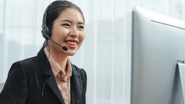 Asian customer support operator wearing headset and microphone working at her desk with laptop. Enthusiastic female employee provide customer service, supportive call center agent helping customers.