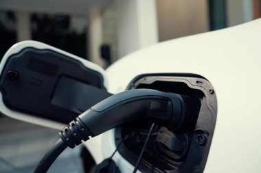 Closeup electric vehicle plugged-in with cable from charging point powered for progressive concept by alternative clean energy rechargeable EV car at home charging station.