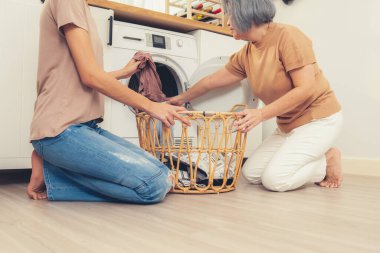 Daughter and mother working together to complete their household chores near the washing machine in a happy and contented manner. Mother and daughter doing the usual tasks in the house.