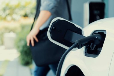 Focus electric car charging at home charging station with blurred progressive man walking in the background. Electric car using renewable clean for eco-friendly concept.