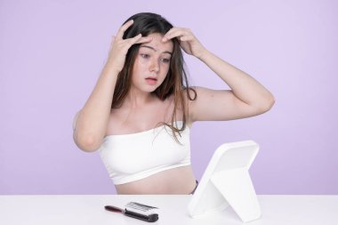 Young charming teenager girl worry about her face pimples on mirror for skincare and acne problem concept. Stress young girl squeezing pimples and pointing fingers on acne on her face.