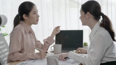 Ofis çalışma alanında birlikte çalışan iki genç hevesli iş kadını. Genç meslektaşlar tartışırken ve dizüstü bilgisayar kullanırken. Modern ofis çalışanları masada birlikte oturuyorlar..