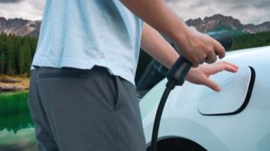 İlerici adam şarj noktasında elektrikli araba yüklüyor, daha temiz bir çevre için temiz ve yenilenebilir enerjiyle çalışan bir EV ile doğada ve dağlarda seyahat ediyor..