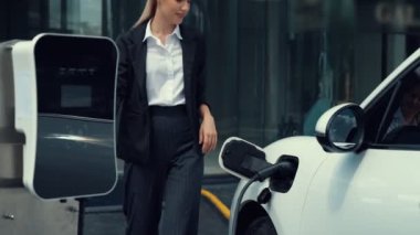 İlerici iş kadını, şehir merkezinde dolaşmadan önce şarj cihazının fişini şarj istasyonundan elektrikli arabasına çekti. Çevre dostu şarj edilebilir araba, sürdürülebilir ve temiz enerjiyle çalışıyor..