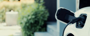 Closeup electric vehicle plugged-in with cable from charging point powered for progressive concept by alternative clean energy rechargeable EV car at home charging station.