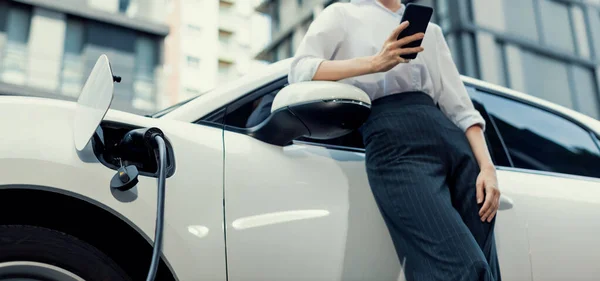 Closeup Progressive Businesswoman Smartphone Leaning Electric Car Charging Station Driving — Fotografia de Stock