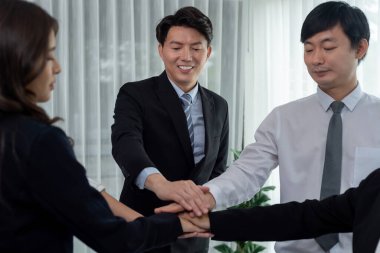 Closeup business team of suit-clad businessmen and women join hand stack together and form circle. Colleague collaborate and work together to promote harmony and teamwork concept in office workplace.