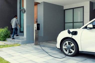 Progressive asian man and electric car with home charging station. Concept of the use of electric vehicles in a progressive lifestyle contributes to a clean and healthy environment.