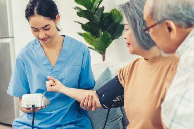 An elderly woman with a contented life having a blood pressure check by her caregiver at home with a smiley face.