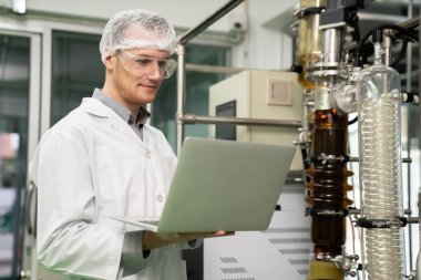 Eczacı bilimadamı CBD yağ çıkarıcısından bilgi kaydetmek için dizüstü bilgisayar ve tıbbi esrar ürünleri üretmek için kullanılan bilimsel bir makine kullanıyor..