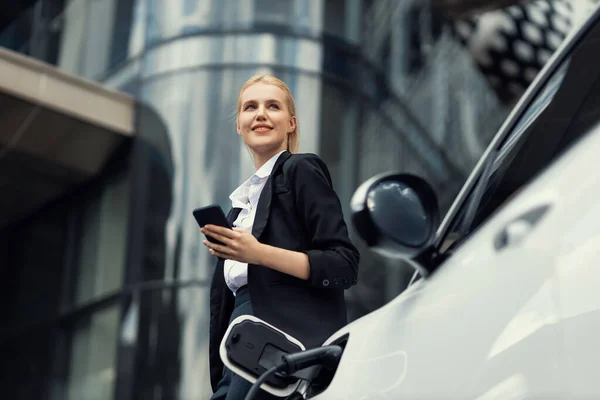 Businesswoman Wearing Black Suit Using Smartphone Leaning Electric Car Recharge — Stok fotoğraf