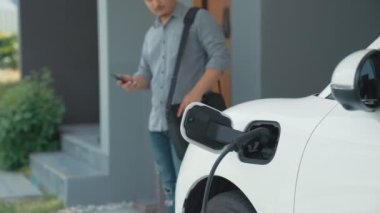 Adamın biri evinde elektrikli araç şarj aletinin fişini çekiyor. İlerici bir yaşam tarzında elektrikli araçların kullanımı, temiz ve sağlıklı bir çevreye katkıda bulunur..