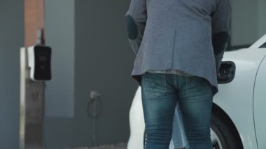 İlerici baba-kız elektrikli araç şarj istasyonundan fiş takıyor. Geleceğin çevre dostu arabası yenilenebilir temiz enerji kaynağıyla çalışıyor..