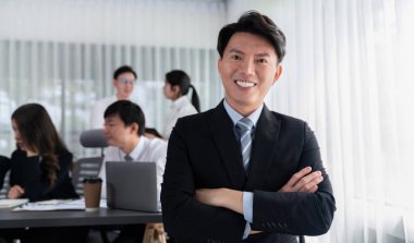 Portrait of focus young successful confident male manager, executive wearing business wear in harmony office arm crossed with blurred meeting background of colleagues, office worker.