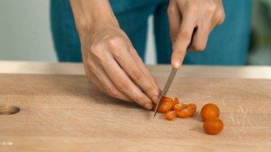 Close up hands holding a knife preparing a contented meal. Sliced tomatoes and other vegetables on the glass dish.