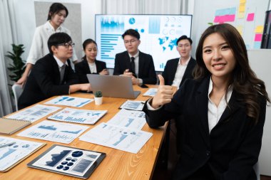 Focus portrait of female manger, businesswoman in the harmony meeting room with blurred of colleagues working together, analyzing financial paper report and dashboard data on screen in background.