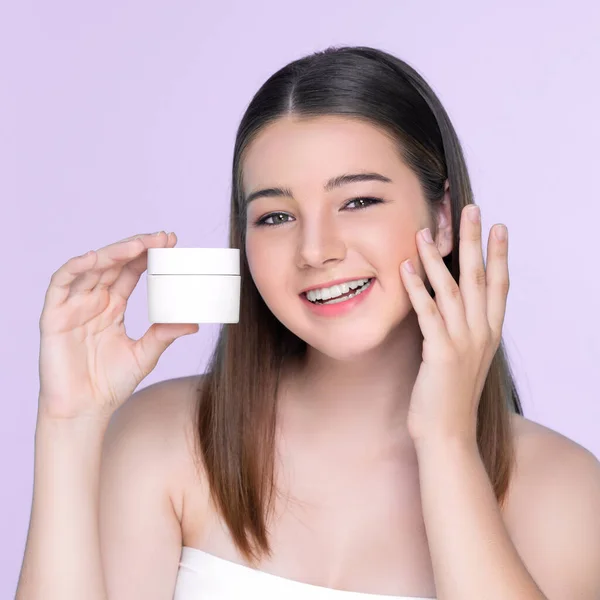 stock image Young charming girl with natural beauty, perfect smooth skin hold lotion, cream, moisturizer jar. Beautiful girl show skincare product smiling on isolated background.