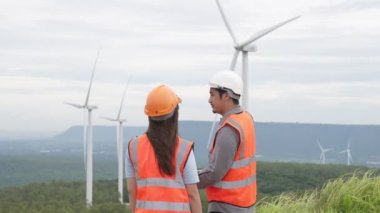 Erkek ve kadın mühendisler kırsal kesimdeki bir tepenin tepesinde ya da dağda rüzgar çiftliğinde çalışıyorlar. Yenilenebilir ve sürdürülebilir enerjinin gelecekteki üretimi için yenilikçi idealler.