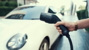 İlerici iş kadını şehir merkezinde dolaşmadan önce şarj cihazından elektrikli arabasına şarj prizi takıyor. Çevre dostu şarj edilebilir araba, sürdürülebilir ve temiz enerjiyle çalışıyor..
