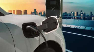 Elektrikli araç, EV araba şehir merkezindeki şarj istasyonunda şarj oluyor. Etrafı yüksek gökdelenlerle çevrili. Çevre dostu yenilikçi temiz enerji kavramı.