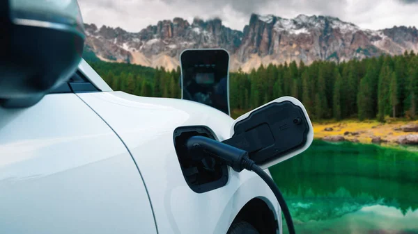 Energy sustainable car power by electro generator drive, recharge battery at charging station with mountain background for progressive travel concept. EV car in nature as symbol for clean environment.