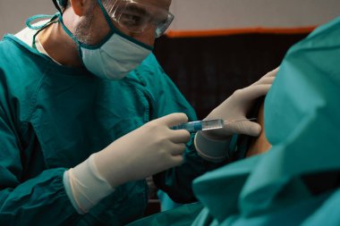 Cerrah, modern cerrahi ekipmanlarla steril ameliyathanede ameliyat yapmadan önce hastaya şırınga enjekte eder. Profesyonel ve kendine güvenen cerrah tarafından yapılan tıbbi ameliyat..