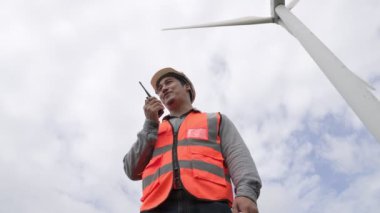Gökyüzü arka planına sahip bir rüzgar türbini üzerinde çalışan mühendis. Yenilenebilir ve sürdürülebilir enerjinin gelecekteki üretimi için yenilikçi bir ideal. Rüzgar türbininden enerji üretimi.