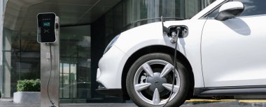 Progressive electric vehicle recharging battery at charging station powered by sustainable clean energy at city residential area. Eco-friendly vehicle concept.