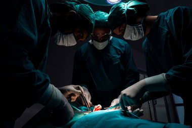 Steril ameliyathanedeki hastaya ameliyat yapan cerrahi ekip. Bir lambanın yaktığı ameliyathanede, profesyonel ve kendinden emin bir cerrahi ekip bilinçsiz bir hastaya tıbbi bakım sağlar..