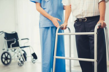 Physiotherapist assists her contented senior patient on folding walker. Recuperation for elderly, seniors care, nursing home.