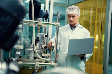 CBD yağ çıkarıcısının yanında dizüstü bilgisayarla çalışan eczacı bilim adamı ve tıbbi esrar ürünleri üretmek için kullanılan bilimsel bir makine.